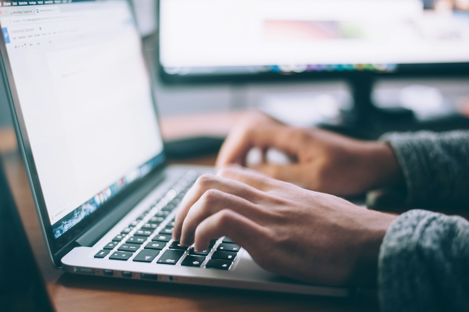 Manos escribiendo en el teclado de un portátil con un documento en blanco abierto