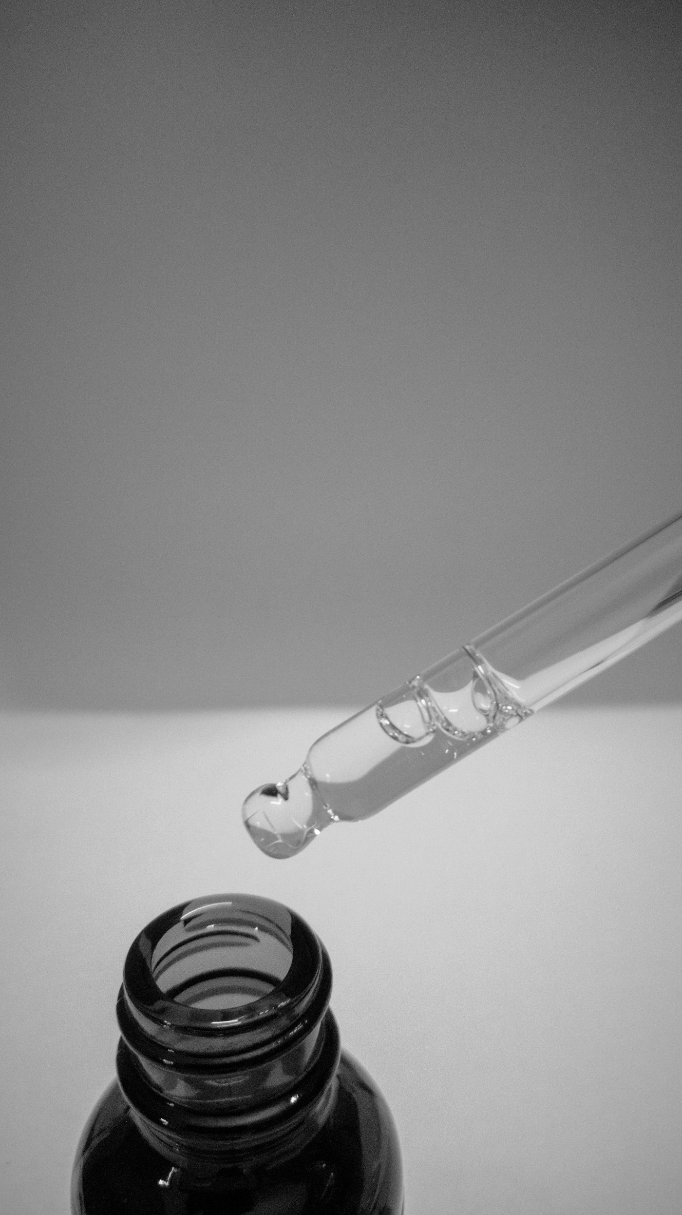 Cuentagotas de vidrio dejando caer una gota sobre la boca del frasco